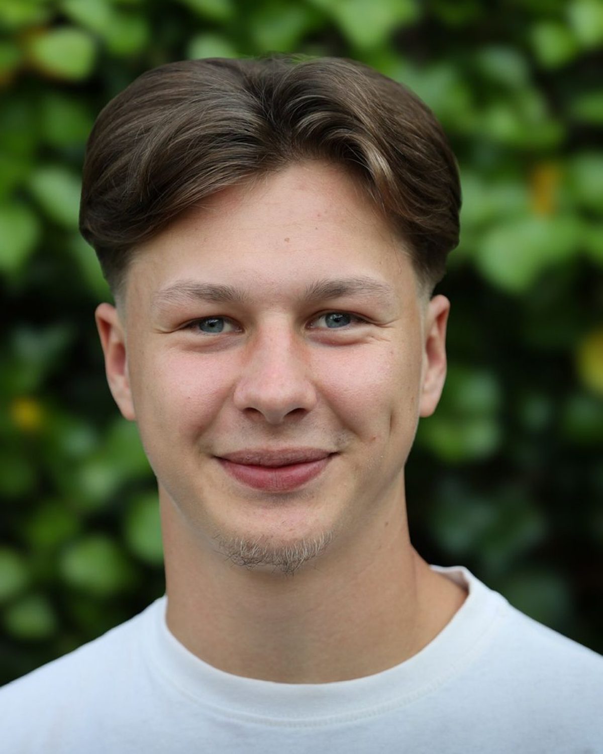 Porträt von Christian Sachs vor einer grünen Hecke